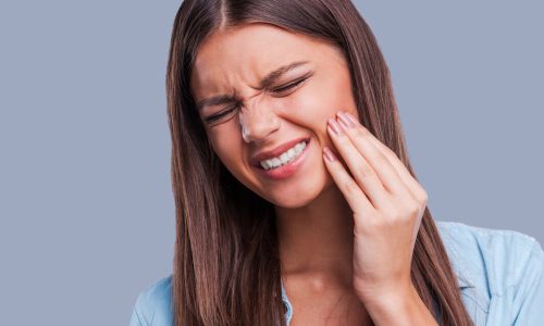 Suffering from toothache. Beautiful young woman suffering from toothache while standing against grey background